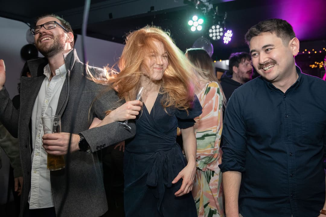 Three people dancing and smiling at a lively indoor party with colourful lights.
