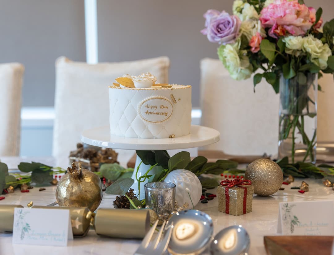White cake with Happy 10th Anniversary on a table with flowers and festive decorations.